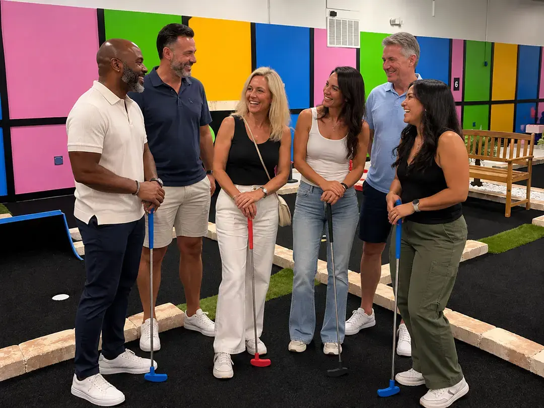 Coworkers smiling with putters at an indoor mini-golf employee appreciation event in Tampa, FL